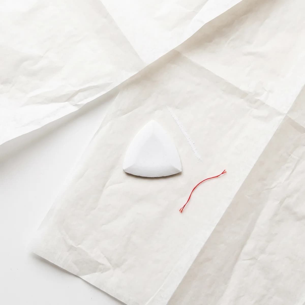 Un gessetto da sarto bianco su carta da modello, accanto a un filo rosso